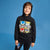 A young boy wearing a black Sonic the Hedgehog graphic hoodie and matching black pants, standing against a solid blue studio background.