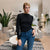 A woman posing in a modern living room setting, wearing a fitted black long-sleeve mock neck top and blue jeans.