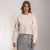 A woman modeling a light cream crewneck sweatshirt paired with a silver sequined skirt, set against a plain light gray studio background.