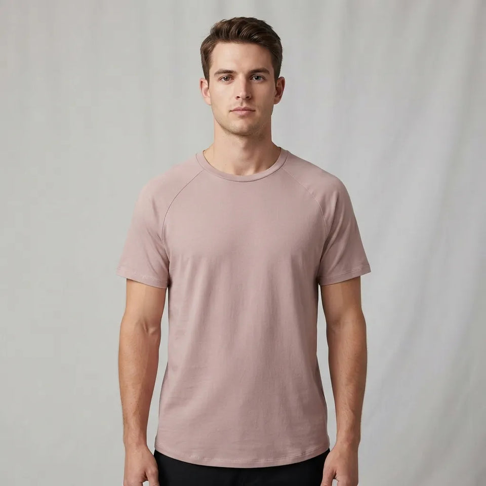A man wearing a short-sleeve crewneck t-shirt in a dusty rose pink color, standing against a neutral light gray studio backdrop.