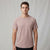 A man wearing a short-sleeve crewneck t-shirt in a dusty rose pink color, standing against a neutral light gray studio backdrop.