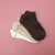 A stack of four low-cut ankle socks in white, beige, and dark brown, arranged diagonally on a solid pink background.
