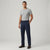 A man modeling navy blue trousers with a light gray t-shirt and brown leather shoes, standing against a light gray studio background.