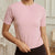 A woman wearing a light pink short-sleeve crewneck athletic top, paired with black bottoms, standing in an elegant indoor setting with white paneled walls.
