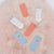 Five baby socks arranged on a fluffy pink faux-fur surface. The set includes two coral-pink socks, two light blue socks with cartoon fish designs, and one white sock with pastel starfish and sea-creature prints.