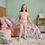 A young girl stands in a child's bedroom wearing a light pink short-sleeve pajama top and matching pajama pants with a small multicolor mermaid and star pattern. She is smiling and holding the sides of a bed with pink bedding and a matching mermaid print blanket.