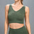 A woman wearing a ribbed knit sleeveless crop top in olive green, paired with matching high-waisted bottoms, shown against a plain gray studio background.