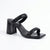 A single black heeled sandal with a square toe, featuring a glossy black block heel and straps embellished with sparkling rhinestones, shown against a plain white background.