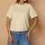 A woman wearing a pale yellow short-sleeve t-shirt with 3D white flower appliquรฉs, paired with blue jeans, set against a warm beige background.