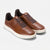 A pair of brown leather low-top sneakers with perforated details, dark brown laces, and thick off-white soles, shown on a light gray background.