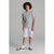 A child model wearing a heather gray short-sleeve t-shirt with a small yellow graphic on the chest, matching light gray shorts, white socks, and green and white sneakers, standing against a neutral gray studio background.