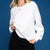 A woman wearing a white crewneck sweatshirt with a large tonal embossed LA Sports logo on the front, paired with a black skirt, set against a solid blue background.