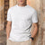 A man wearing a white short-sleeve henley t-shirt with a three-button placket, leaning against a rustic stone wall.
