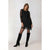 A woman modeling a black long-sleeve mini dress with sheer mesh sleeves and a sheer hem overlay, paired with black tights and black knee-high boots, against a plain light gray studio background.