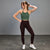 A woman posing in a studio setting wearing a green marled sports bra and dark burgundy high-waisted leggings with white sneakers.