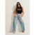 A woman posing in a studio setting wearing a black sleeveless crop top with 'SWEET SUMMER' text and graphic details, paired with light-wash wide-leg denim jeans and dark sunglasses.