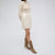 A model is shown from the side wearing a cream ribbed knit long-sleeve top and a matching cream sequined mini skirt, paired with taupe suede ankle boots, against a light gray studio background.