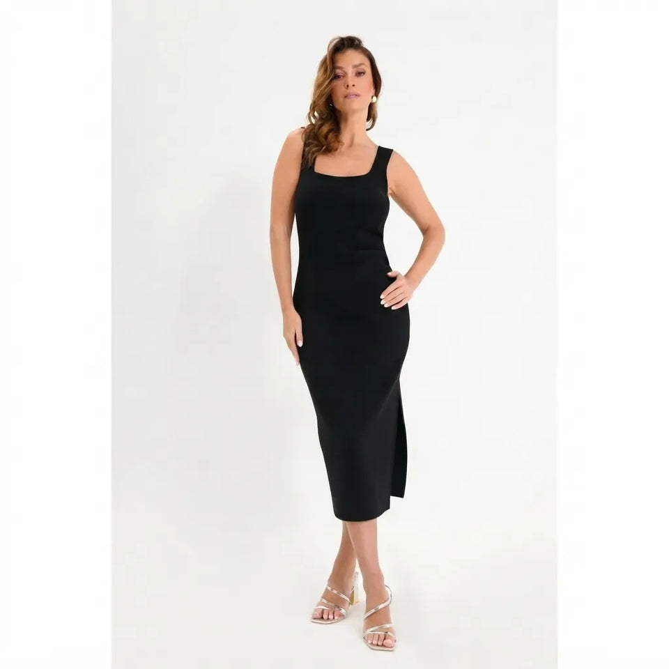 A woman modeling a sleeveless black midi dress with a square neckline and side slit, paired with clear high-heeled sandals, against a plain white studio background.