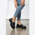 A person wearing black leather platform loafers with a horsebit detail, paired with light blue cropped jeans, shown from the waist down against a neutral studio background.