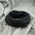 A black infinity scarf made of soft, textured fabric, styled on a light gray draped background.