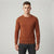 A man wearing a rust-brown long-sleeve crewneck sweater and dark gray jeans, standing against a light gray studio background.