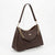 A dark brown pebbled leather hobo shoulder bag with a gold-tone chain link accent and a small gold logo plate, displayed on a clear acrylic stand against a white background.