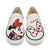 A pair of white slip-on canvas sneakers featuring Minnie Mouse graphics, including a black and red printed character on the left shoe and a red polka-dot bow design with the cursive 'Minnie' script on the right shoe.