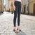 A person wearing slim-fit black skinny jeans and black strappy heeled sandals, standing on a cobblestone street in a European-style town with buildings on both sides.