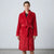 A woman wearing a plush red bathrobe with a tie belt, standing against a light gray studio background.