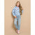 A young girl with long blonde hair stands against a solid beige studio background, wearing a light blue hooded sweatshirt with black polka dots and a pink flamingo graphic, paired with light-wash blue jeans and pink boots.