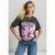 A woman modeling a dark charcoal gray graphic t-shirt with a pink and white retro car design and the text 'THE REACHING ZONE ROAD SPEED Club'. She is wearing blue jeans and standing against a textured gray concrete wall.