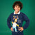 A smiling boy with curly brown hair wearing a navy blue crewneck sweatshirt featuring a Homer Simpson Christmas graphic, posed against a solid green studio background.