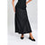 A model wearing a black satin midi skirt with a subtle sheen, paired with a black buttoned top and black pointed-toe slingback heels, set against a light gray studio background.