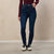 A model wearing dark blue high-waisted skinny jeans, a burgundy ribbed long-sleeve top, and white sneakers, standing against a textured beige wall.