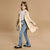 A young girl models a beige double-breasted trench coat over a white patterned top and blue flared jeans, styled with black flats and a small gray handbag against a solid beige studio background.