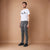 A man modeling a white graphic t-shirt, gray acid-wash skinny jeans, and black sneakers against a solid tan studio backdrop.