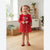 A young girl with blonde pigtails stands in a bright room wearing a red long-sleeve dress with a floral pattern and a cartoon character graphic on the chest, paired with red shoes.