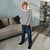 A young boy stands in a living room wearing a black and white horizontally striped long-sleeve shirt, dark blue jeans, and black sneakers.