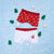 Two pairs of children's boxer briefs laid flat on a light blue textured background with small green tree and white star props. The top pair is red with a beige holiday pattern, and the bottom pair is white with a red waistband and a small holiday mug graphic.