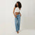 A woman modeling light-wash wide-leg blue jeans with a white ribbed crop top, standing against a plain off-white studio background.