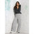 A woman posing in a dark gray knit sweater and light gray wide-leg cargo sweatpants against a white brick wall background.