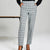 A person wearing slim, cropped plaid trousers in a light gray and white windowpane pattern, paired with a black long-sleeve top and black high heels, standing against a light gray studio background.