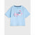 A light blue short-sleeve t-shirt for kids, featuring a 'I'm full of bloom' graphic with pink flowers and a black heart on the front, displayed against a light gray background.