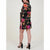 A woman modeling a short black wrap-style dress with a vibrant multicolor floral print, shown from a side-back angle against a plain light background.