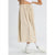 A model wearing a beige pleated midi skirt with an elastic waistband and drawstring, styled with white socks and white sneakers against a light gray studio background.