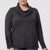 A woman wearing a dark charcoal gray cowl neck sweater with decorative buttons on the cuffs, shown from the chin down against a light gray background.