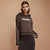 A woman modeling a dark brown cropped hoodie with 'PRAGUE' printed in yellow across the chest and a cream stripe down the sleeve, paired with a black skirt, against a solid beige background.