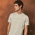 A man wearing a light beige crew-neck t-shirt with the text 'ANTI-SOCIAL BEHAVIOUR' printed in black across the chest, posed against a textured brown background.