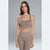 A woman modeling a matching taupe activewear set consisting of a scoop-neck sports bra and high-waisted leggings, set against a neutral gray studio background.