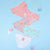 Four pairs of women's briefs in pastel colors are arranged on a light blue background with small decorative props. The briefs include pink, mauve, mint, and white options, each featuring a small house graphic on the front.